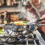 En un wok d'acer inoxidable amb recobriment antiadherent es cuina aliments de colors en una estufa de gas, emetent vapor.