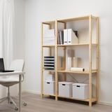 Oficina a casa amb prestatgeria d'emmagatzematge de fusta clara IVAR, amb caixes blanques, llibres i gerros al costat d'un escriptori amb una cadira blanca.
