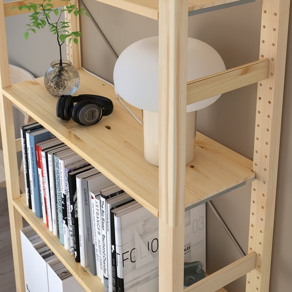 Prestatgeria de fusta clara amb múltiples prestatges que mostren llibres, auriculars, una petita jardinera i una làmpada, que proporciona emmagatzematge i organització versàtils.