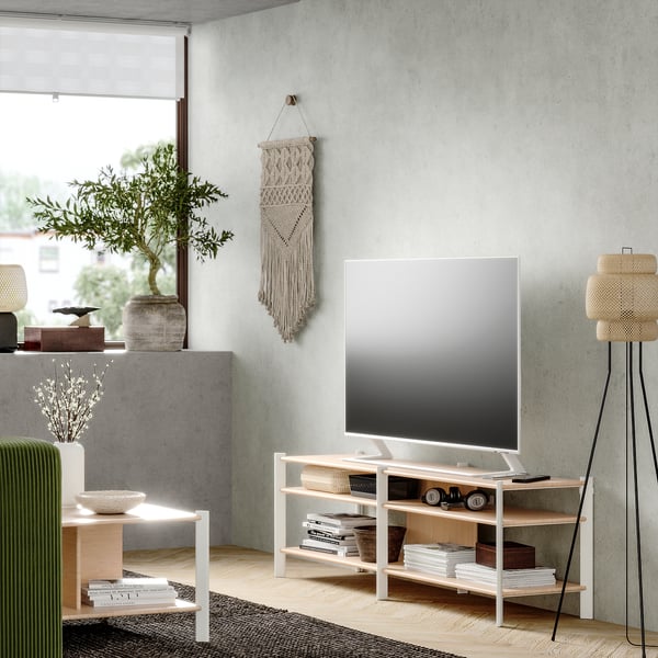 Sala d'estar moderna amb suport de TV blanc JÄTESTA, prestatges de bambú, disseny elegant, televisor de pantalla plana, cadira verda, planta d'interior, catifa teixida.