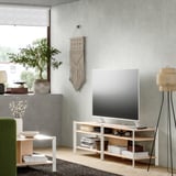 Sala d'estar moderna amb suport de TV blanc JÄTESTA, prestatges de bambú, disseny elegant, televisor de pantalla plana, cadira verda, planta d'interior, catifa teixida.