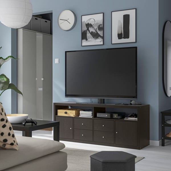 Sala d'estar moderna amb suport de TV fosc KALLAX, gran pantalla plana, sofà gris, taula de centre i paret blava.