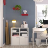 Oficina a casa amb prestatge KALLAX, llibres, llum brillant, prestatges de plantes vermelles, rellotge, escriptori, ordinador. Paret blava, terra de fusta.