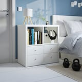 Unitat d'emmagatzematge KALLAX blanca al costat del llit, amb llibres, auriculars i llum. Més petit que el llit, s'adapta perfectament a la cantonada.