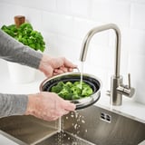 La persona renta el bròquil en un lavabo amb un colador plegable connectat a una aixeta moderna.