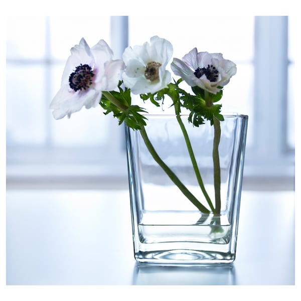 Un gerro de vidre transparent KLOTTRIG amb flors blanques prop d'una finestra.