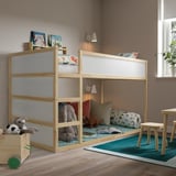 Habitació infantil amb llit KURA, fusta clara, peluixos, coixins de colors, catifa blava i llum natural.