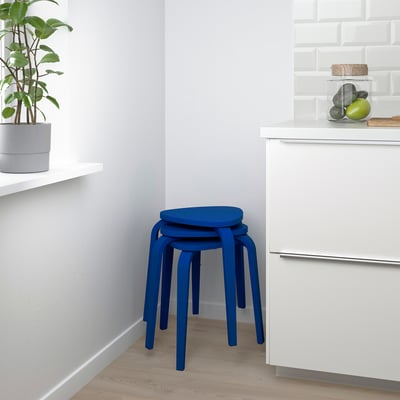 Tamboret blau apilat sobre taulell de cuina blanc, amb test de plantes i gerra de fruita; seients i emmagatzematge funcionals.