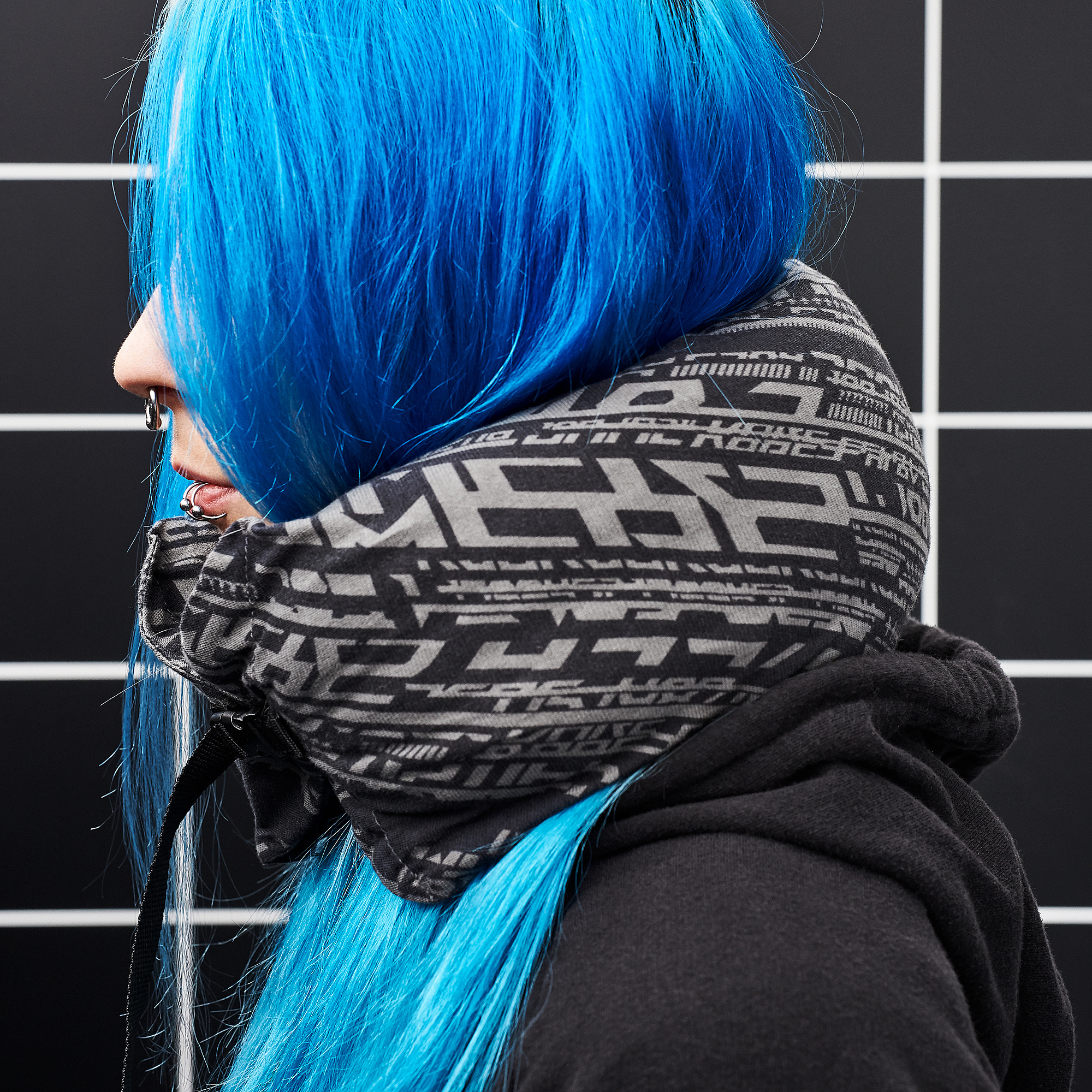 Una persona porta un coixí blau LÅNESPELARE amb un disseny de text negre sobre una dessuadora amb caputxa negra.
