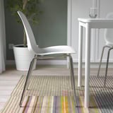 Configuració moderna del menjador amb cadires blanques, taula, catifa de ratlles i planta.
