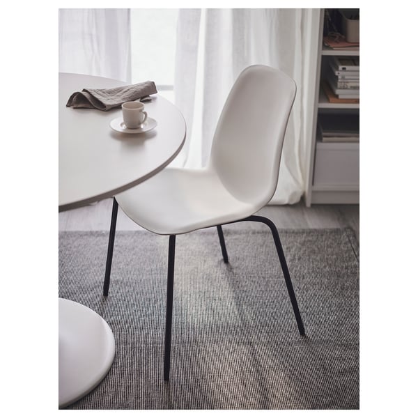 Cadira LIDÅS blanca minimalista amb respatller corbat i potes fines prop d'una taula blanca amb una tassa.