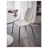 Cadira LIDÅS blanca minimalista amb respatller corbat i potes fines prop d'una taula blanca amb una tassa.