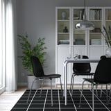 Menjador modern: elegants cadires negres LIDÅS, potes cromades, taula de vidre, prestatgeria blanca, llum penjant elegant. Catifa de quadres foscos.