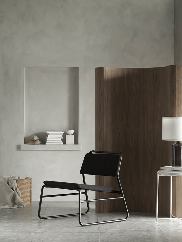 Habitació moderna i minimalista amb butaca negra LINNEBÄCK, mampara de fusta, prestatgeria blanca amb llibres i parets grises.