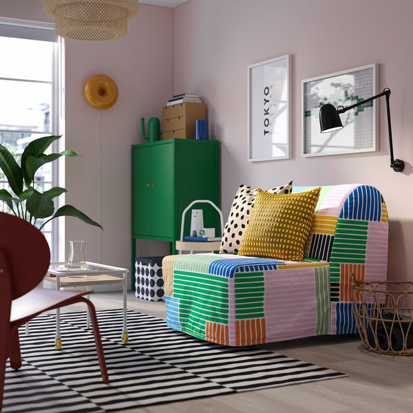 El sofà amb estampats brillants i colorits domina l'habitació amb parets pastel, armari verd i art de Tòquio.
