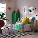 El sofà amb estampats brillants i colorits domina l'habitació amb parets pastel, armari verd i art de Tòquio.