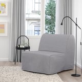 Sala d'estar moderna i minimalista. Cadira-llit de lycksele gris, elegant taula auxiliar negra, llum de peu. Gran finestral amb cortines, terra de fusta clara.