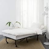 Cadira-llit blanca minimalista, marc negre, llum de peu, planta, llibre.