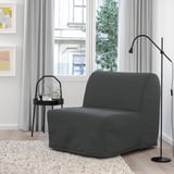 Cadira-llit grisa moderna i compacta amb disseny minimalista, col·locada a prop de la finestra, catifa grisa i petit suport per a plantes. Versàtil i estalviador d'espai.