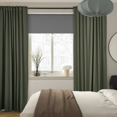 Dormitori modern amb grans cortines MAJGULL de color verd fosc, llit de peluix, llum blanca i branques decoratives.