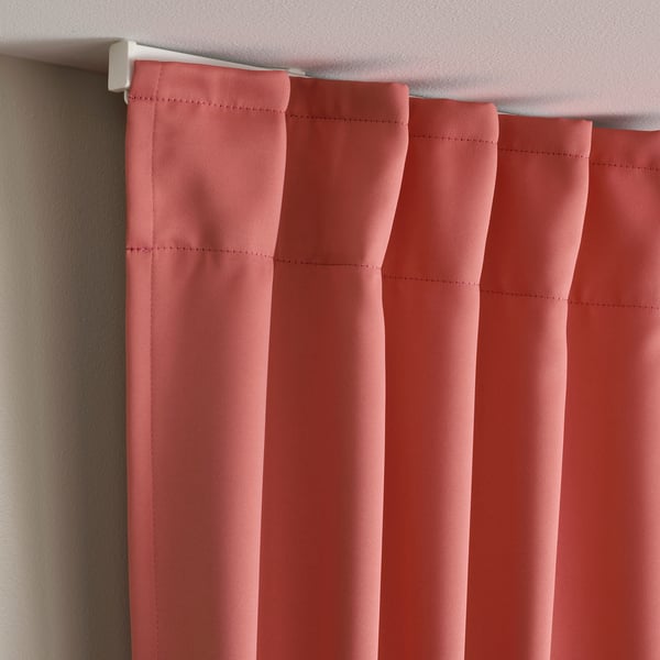 Les cortines vermelles que enfosqueixen l'habitació amb plecs pengen d'una vareta blanca, proporcionant privadesa i control tèrmic.