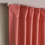 Les cortines vermelles que enfosqueixen l'habitació amb plecs pengen d'una vareta blanca, proporcionant privadesa i control tèrmic.