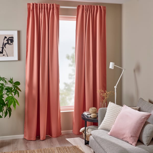 Cortines rosades que enfosqueixen l'habitació, plisades, fins al terra, polièster reciclat, afegint color, privadesa i control de la llum. Una cadira i un llum al seu costat.