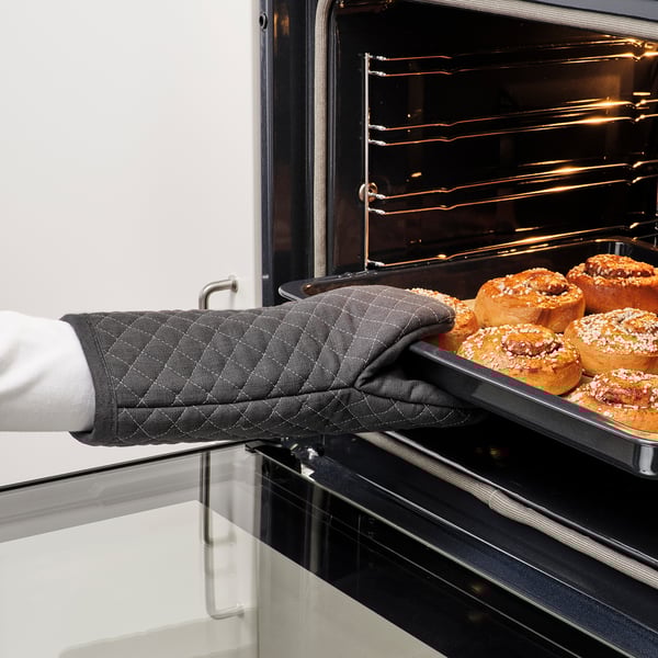 Persona que utilitza el guant de forn MARIATHERES per treure la safata de pastissos daurats del forn.