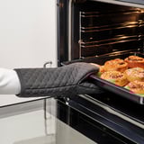 Persona que utilitza el guant de forn MARIATHERES per treure la safata de pastissos daurats del forn.