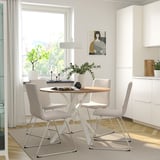 Menjador modern amb taula rodona blanca i 4 cadires grises. Potes d'acer, col·locació central, decoració.