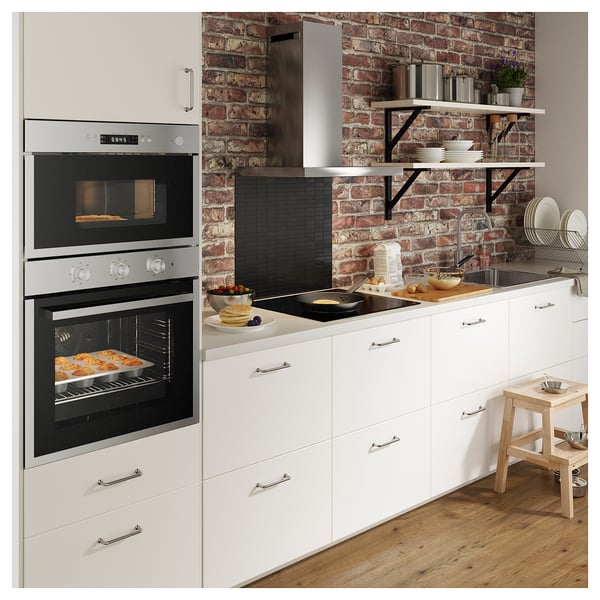 Cuina moderna amb armaris blancs, backsplash de maó, forn d'acer inoxidable, electrodomèstics de taulell, tamboret de fusta i plats.