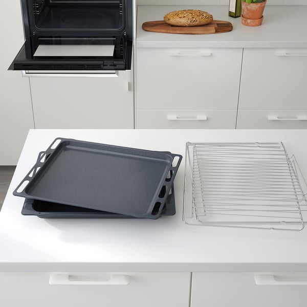 Les safates de forn negres descansen sobre un taulell blanc prop d'un forn obert, amb una reixeta de refrigeració al costat.