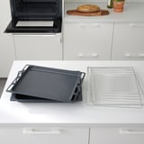 Les safates de forn negres descansen sobre un taulell blanc prop d'un forn obert, amb una reixeta de refrigeració al costat.