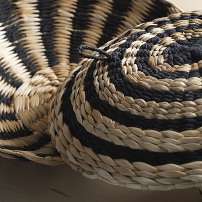 Dos tapissos rodons teixits a mà, un amb ziga-zagues negres, l'altre amb espirals negres, fets de fibres de plàtan i cotó.