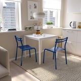 Conjunt de menjador modern i lluminós amb taula blanca i cadires blaves contra un gran finestral. Compacte però elegant, que s'adapta perfectament a la sala petita i lluminosa.