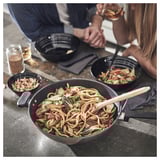 Dues persones compartint àpat amb fideus i bols al wok. Sopar informal en tons foscos.