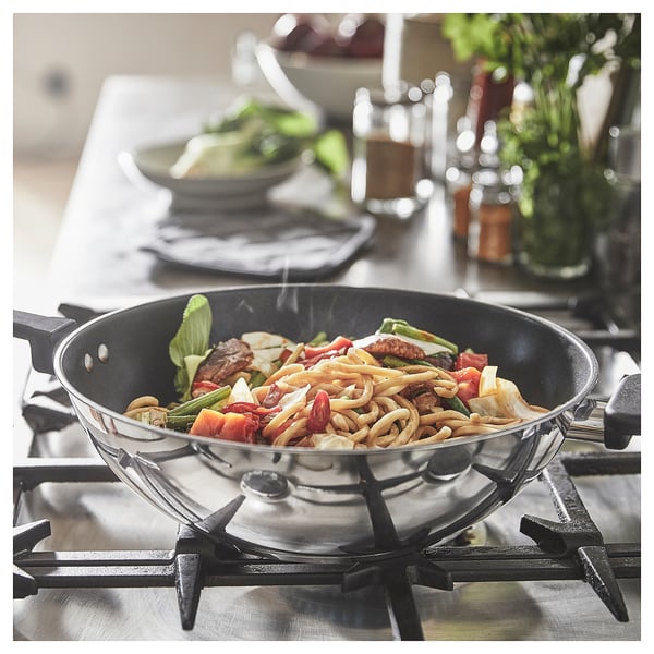 Wok d'acer inoxidable amb recobriment antiadherent cuinant sofregits de colors a la cuina. Mànec addicional fàcil d'aixecar, disseny modern.