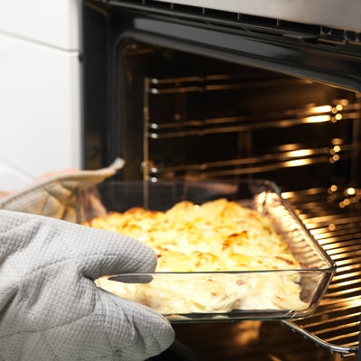 Persona que porta un guant de forn sostenint un plat de vidre de menjar al forn, traient del forn.