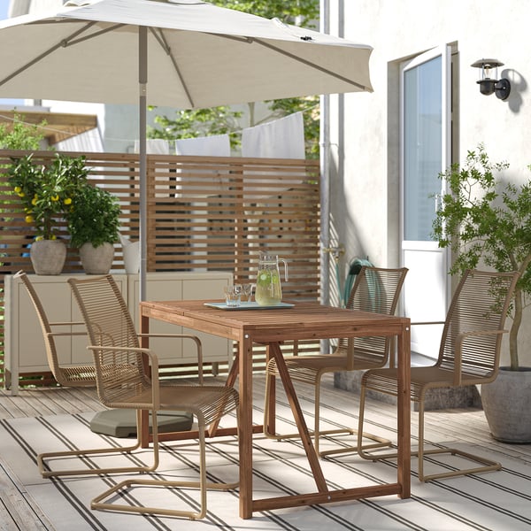 Taula i cadires d'exterior NÄMMARÖ petites. Grans paraigües, còmodes seients encoixinats. Envoltat de plantes en test, a prop de l'entrada d'una casa.