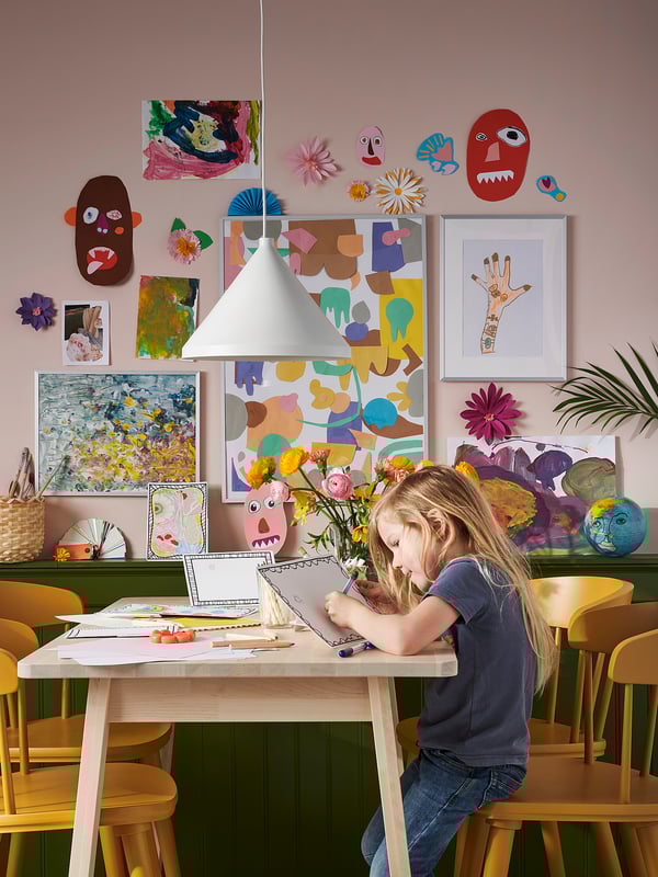 Un nen dibuixant a una taula NORRÅKER de bedoll clar amb cantonades arrodonides en una habitació de colors amb decoracions artístiques a les parets verdes.