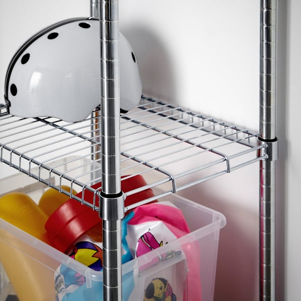 Els contenidors d'emmagatzematge de plàstic transparent plens de joguines de colors es troben a les prestatgeries inferiors d'una rebenta cromada. Un casc blanc descansa a la prestatgeria superior.