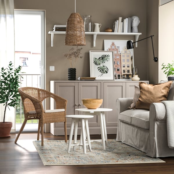 Sala d'estar moderna amb catifa blau clar ONSEVIG, cadires de vímet, sofà gris, tauletes laterals blanques i armari de fusta amb decoracions.