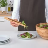 Persona que utilitza pinces de bambú per servir amanida d'un bol en un plat. Les pinces trien eficaçment ingredients específics d'amanides.