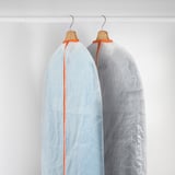 Dos vestits amb fundes protectores amb llaços taronges pengen perfectament en un armari.
