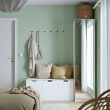 Dormitori modern amb armari PAX blanc, cortines transparents, jaquetes lleugeres, cistella i llit amb manta verda.