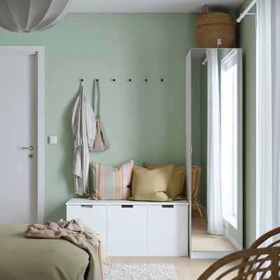 Dormitori modern amb armari PAX blanc, cortines transparents, jaquetes lleugeres, cistella i llit amb manta verda.