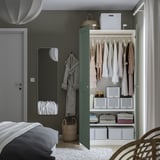 Dormitori amb armari obert: roba, caixes, cistelles, mirall al costat de la porta.