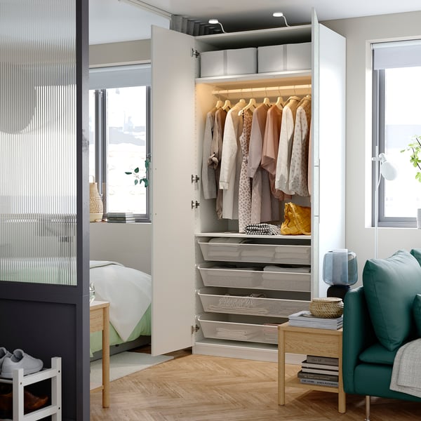 Habitació moderna amb armari PAX blanc amb roba organitzada, cistelles d'emmagatzematge i il·luminació integrada.