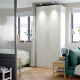 Dormitori modern amb armari PAX floral blanc, finestres, cadira verda, taula de fusta.