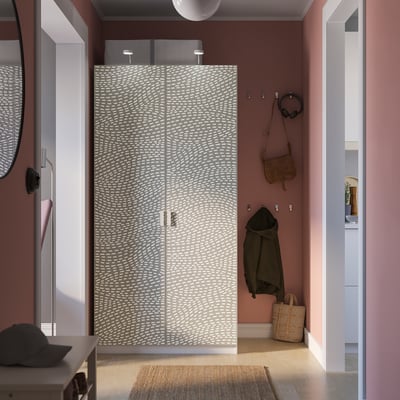 Dormitori modern amb armari PAX estampat, parets roses, catifa teixida i objectes personals.